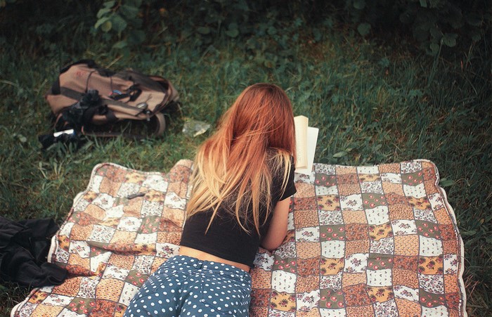 Woman reading a book on a picnic blanket outdoors