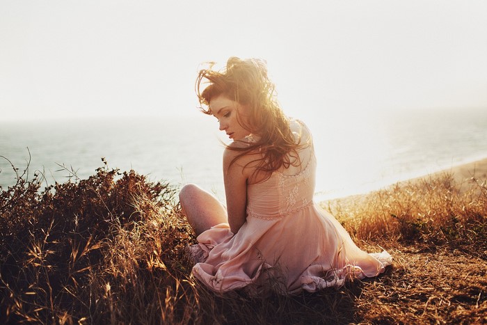 Woman in a dress sitting on a cliff overlooking the ocean