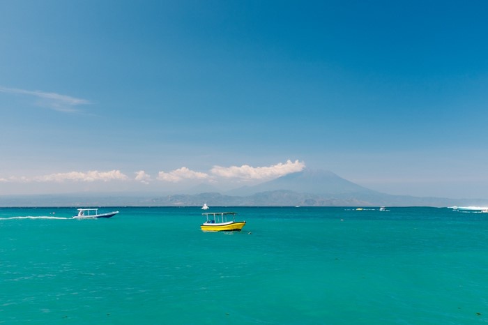 Boats on turquoise water with distant volcano under blue sky