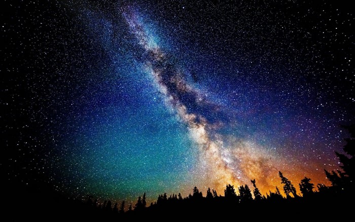 The Milky Way galaxy over a silhouetted forest at night