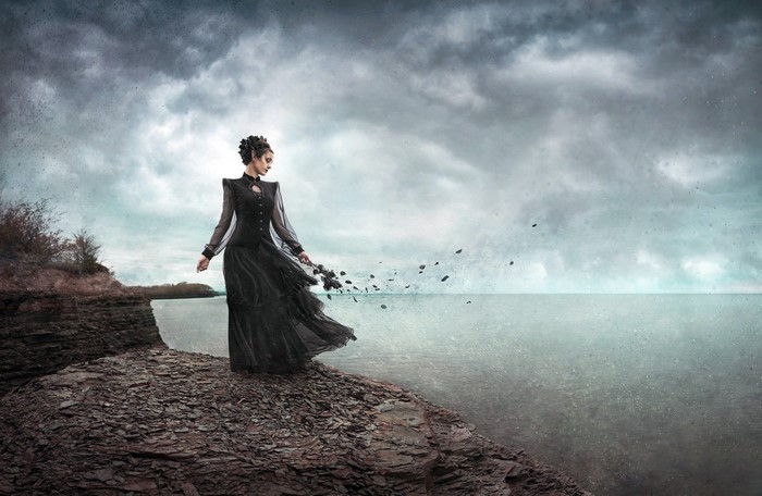 Woman in black dress by the sea under cloudy sky