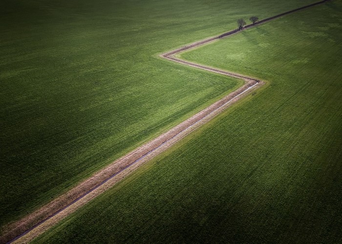 Aerial view of a zig-zagging ditch through a green field