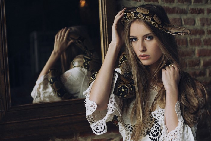 Woman with a snake around her neck in front of a mirror