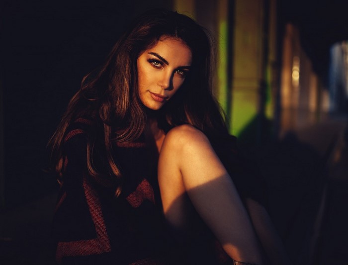 Woman with brown hair sitting in darkness with dramatic lighting