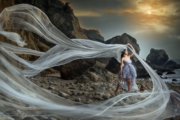 Woman in a dress on a rocky beach with flowing fabric