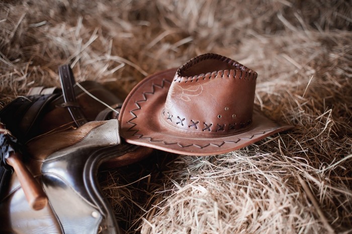 Brown leather cowboy hat and saddle on hay