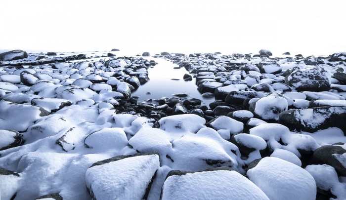 Snow-covered rocks on a frozen shore with calm water