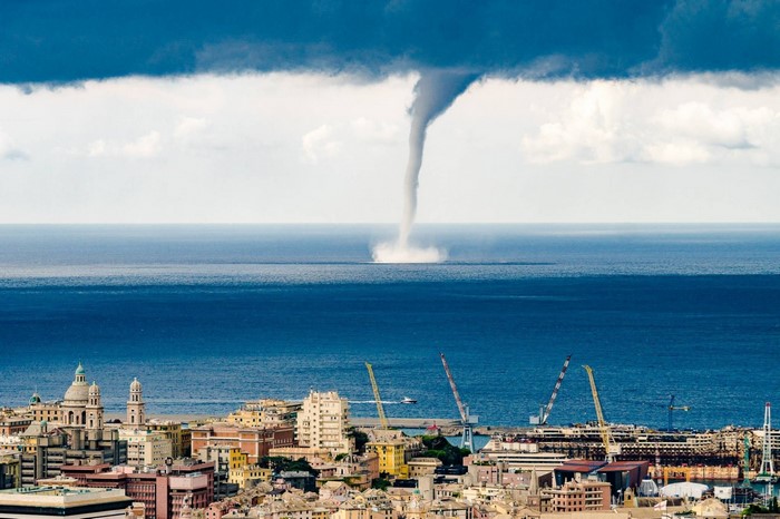 Tornado over the sea near a cityscape with cranes