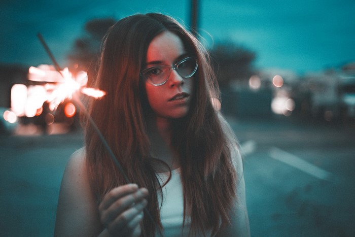 Woman with glasses holding a sparkler outdoors