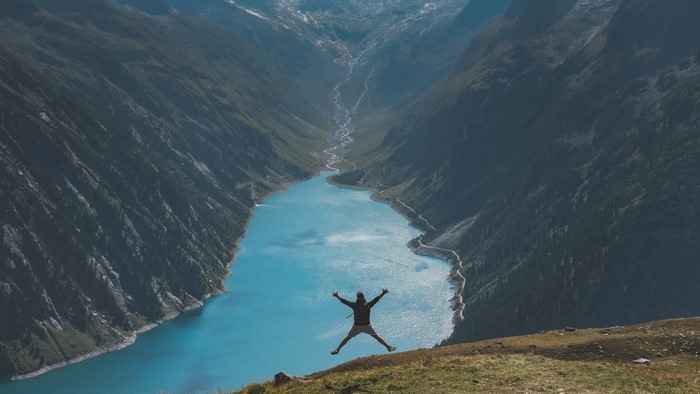 Man jumping over a turquoise lake in the mountains