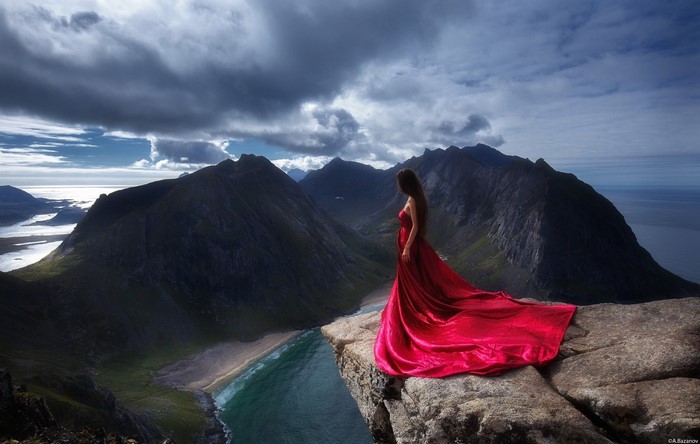 Woman in red dress on cliff overlooking mountains and sea