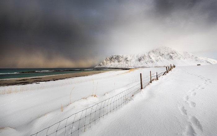 Snowy beach with mountains and a fence