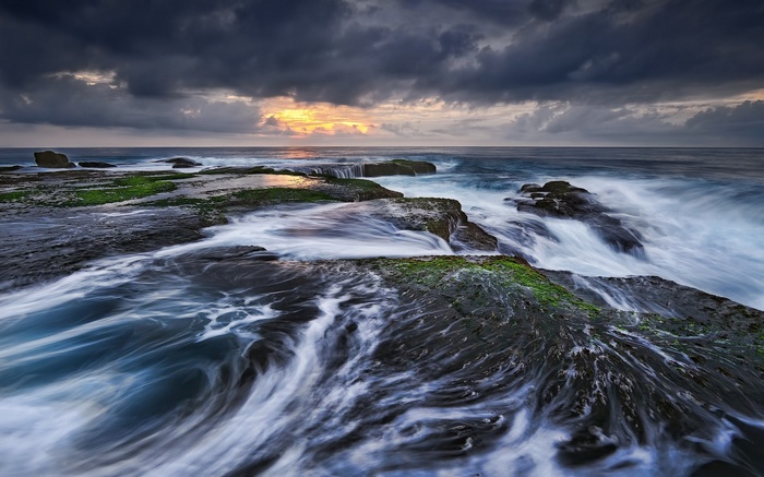 Waves crashing on mossy rocks at sunset