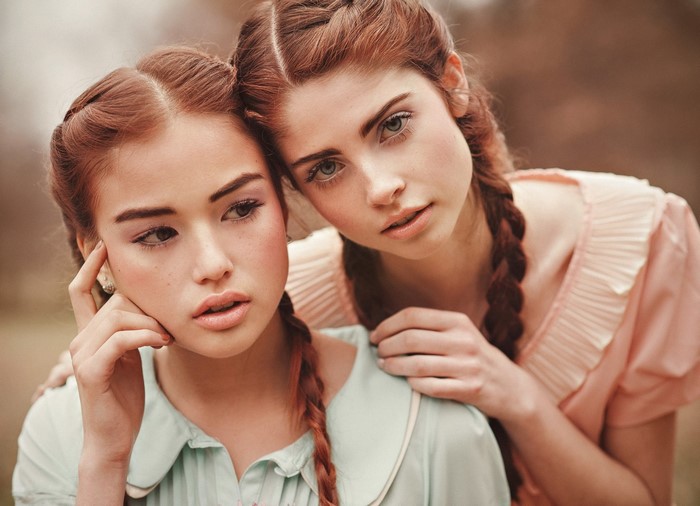 Two young women with braided hair in pastel dresses