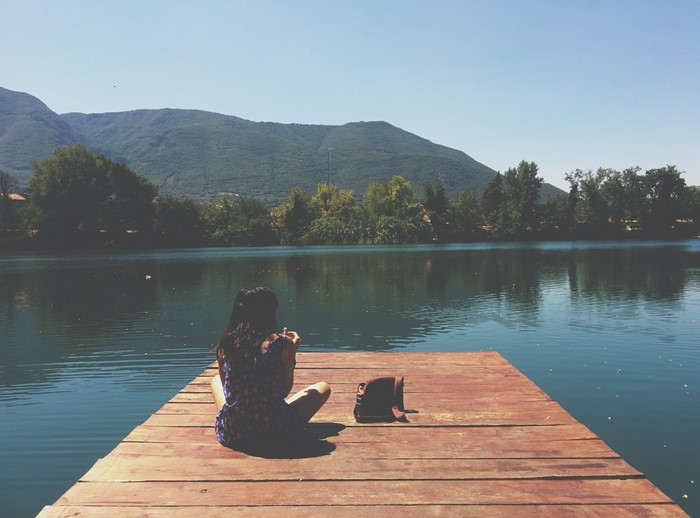 Woman sitting on a pier by a lake with mountains