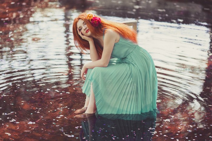 Woman with red hair sitting in water with flowers