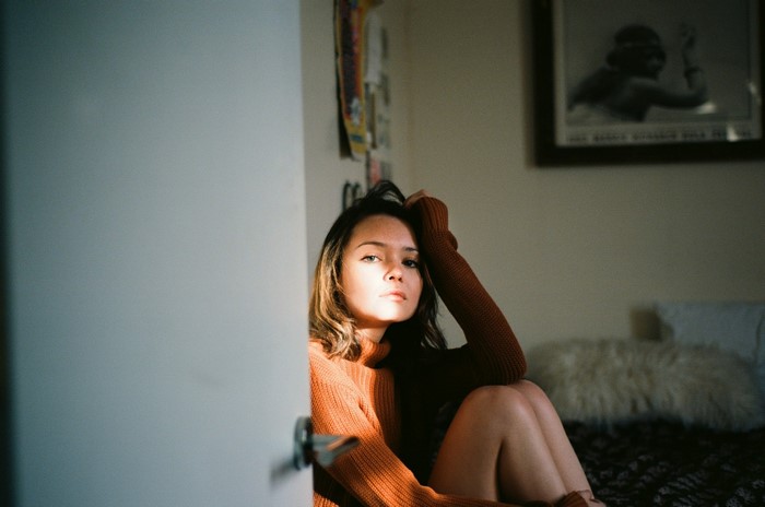 Woman in orange sweater sitting on bed