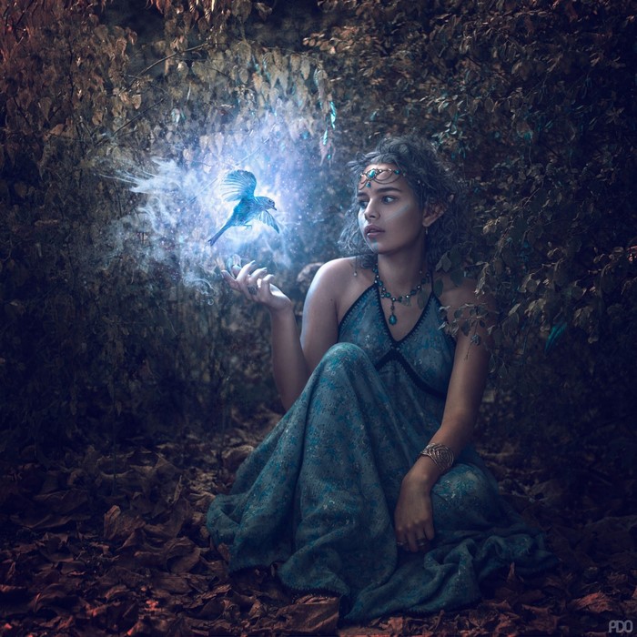 Fantasy girl with glowing blue bird in forest