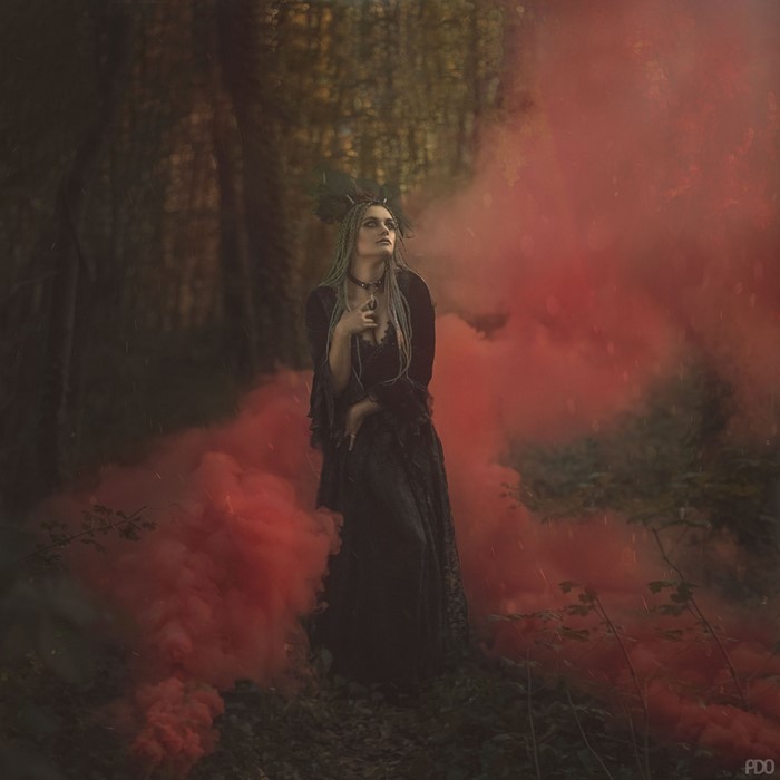 Woman in black dress with red smoke in forest
