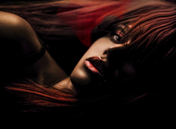 Woman with red hair and red lipstick in darkness