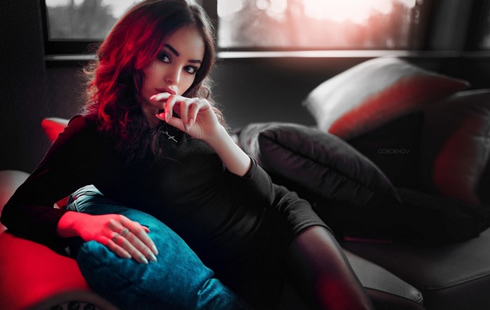 Woman in black dress on a couch with red lighting