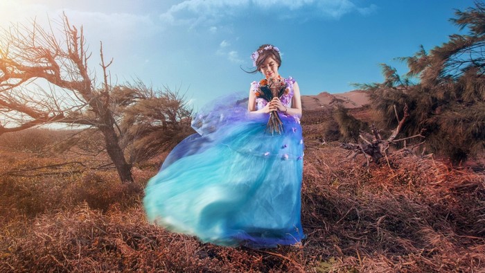 Woman in a flowing blue and purple dress holding flowers