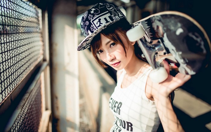 Asian woman wearing a hat and tank top holding a skateboard