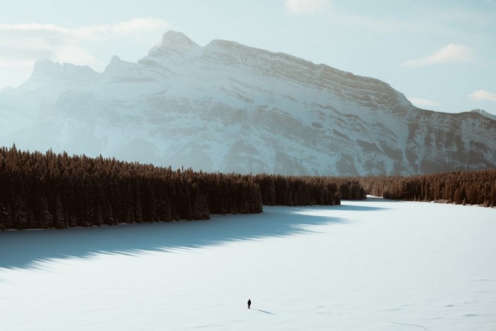 Lone figure on a frozen lake with snow-capped mountains