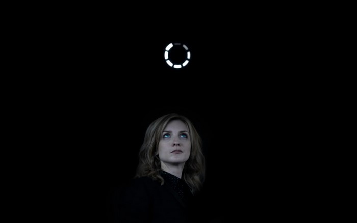 Woman looking up at a circular light in darkness
