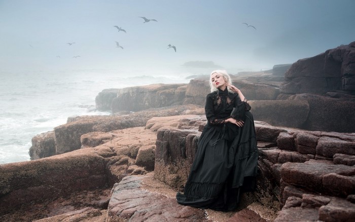 Woman in black dress on rocky coast with seagulls