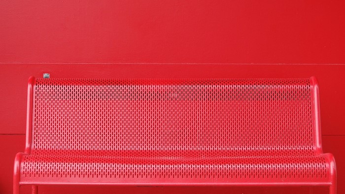 Red perforated bench against a red wall