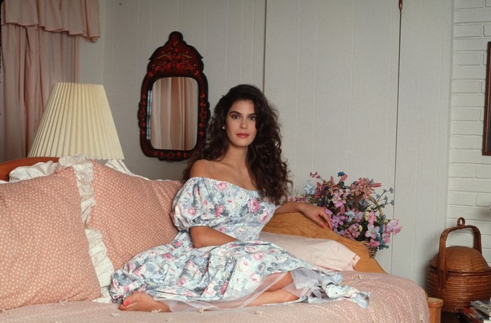 Teri Hatcher in a floral dress sitting on a bed