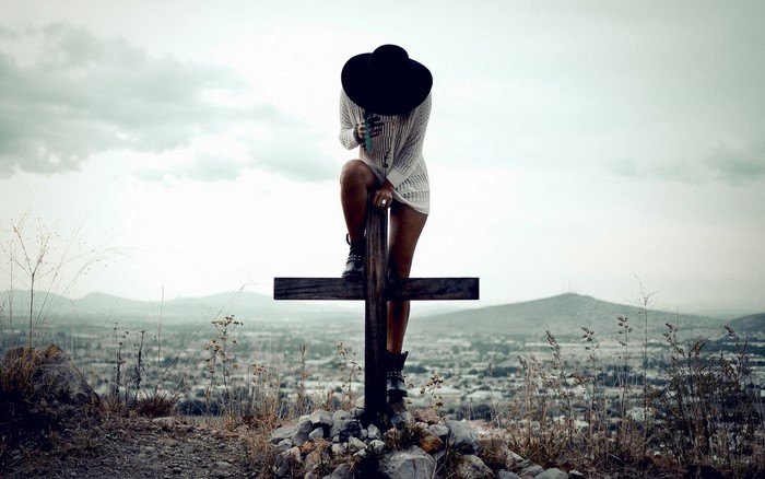 Woman in hat on a cross overlooking a landscape