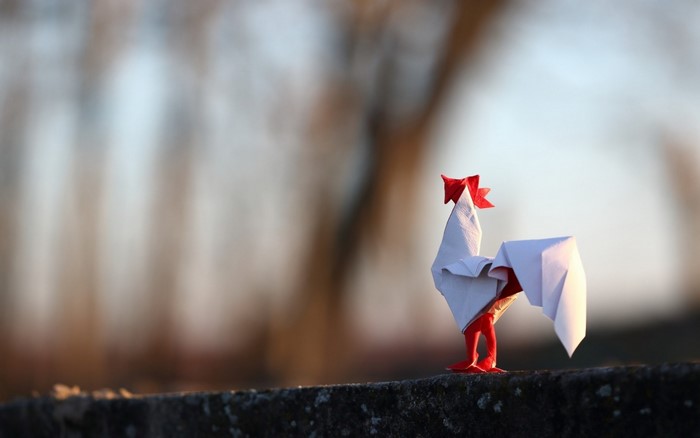 Origami rooster with red comb and legs in sunlight