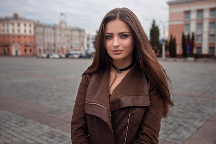 Woman with long brown hair wearing a brown jacket and choker