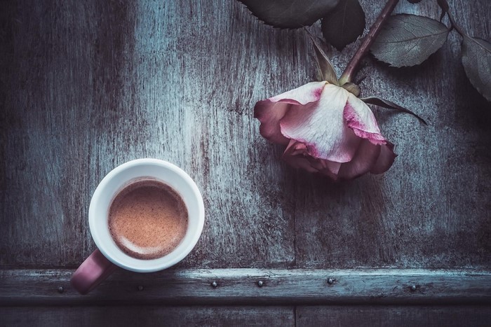 Espresso cup and pink rose on a wooden surface