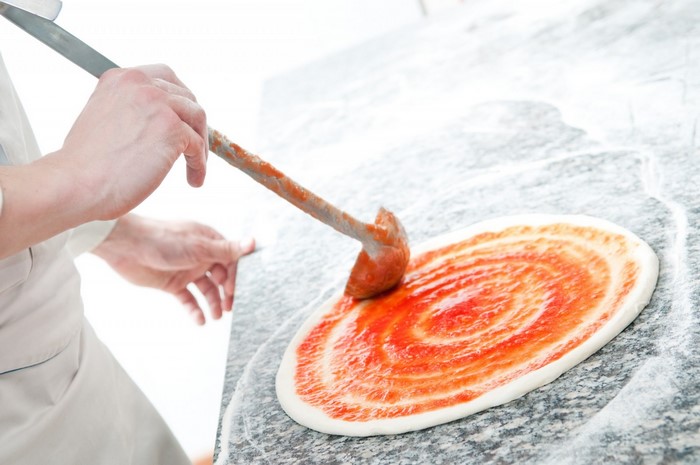 Chef spreading tomato sauce on pizza dough