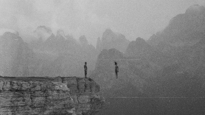 Two figures on a cliff edge in misty mountains