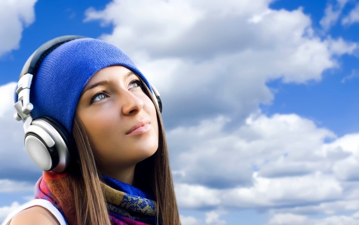Woman wearing headphones and blue hat looking up at clouds