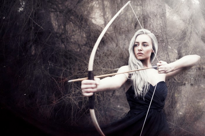 Woman with bow and arrow in dark forest