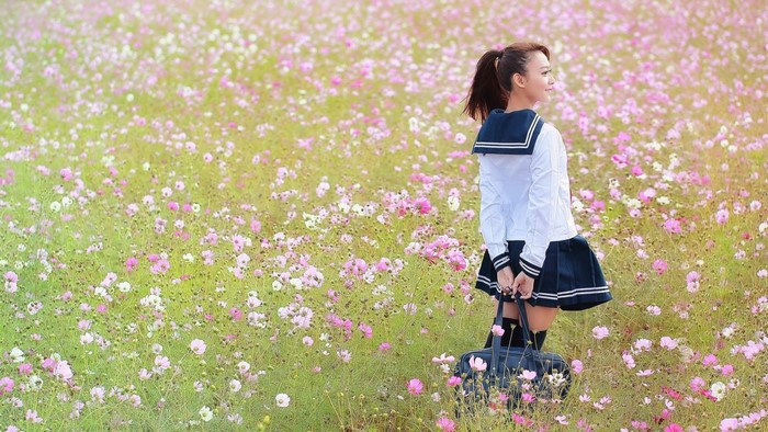 Young woman in school uniform in a field of flowers