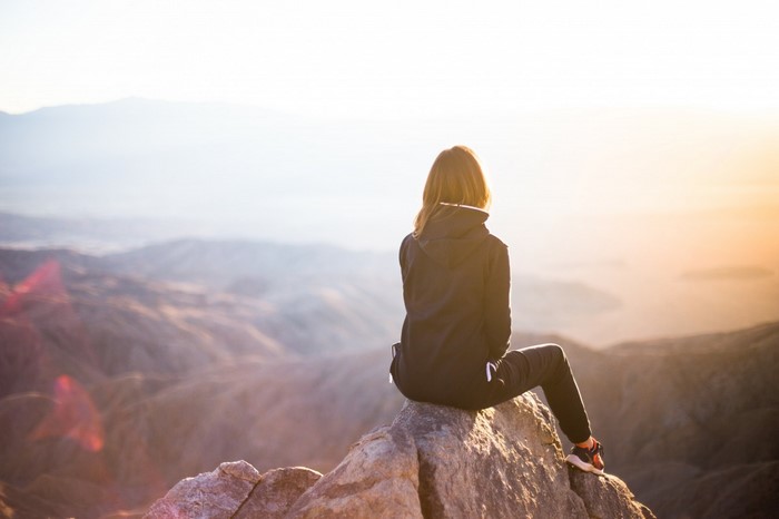 Woman sitting on a rock overlooking mountains at sunrise