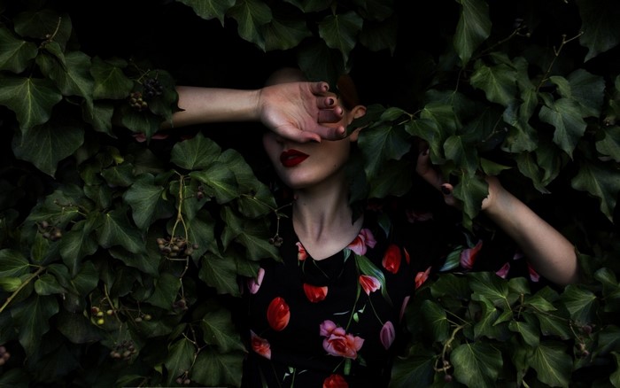 Woman in floral dress hiding face among green leaves