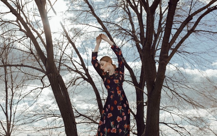 Woman in floral dress with arms raised among trees