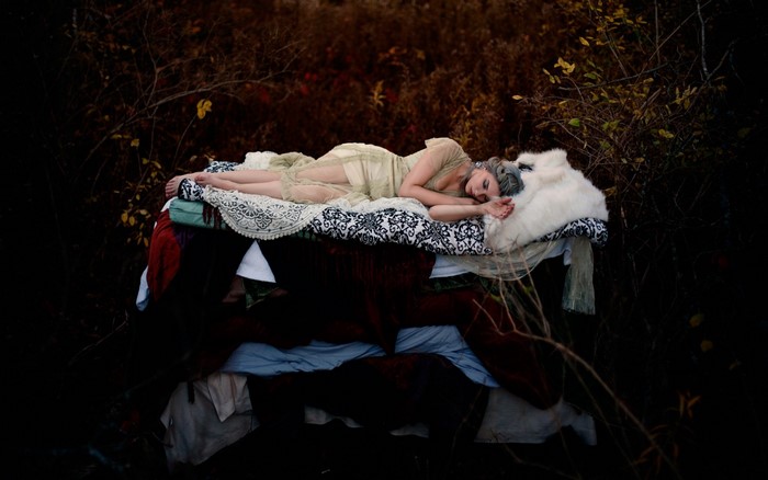Woman sleeping on a bed of blankets in a dark forest