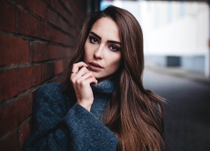 Woman in a blue sweater leaning against a brick wall