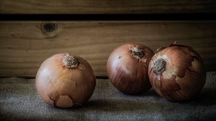 Three onions on a burlap surface with a wooden background
