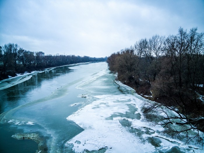 Frozen river with trees on the banks under a cloudy sky
