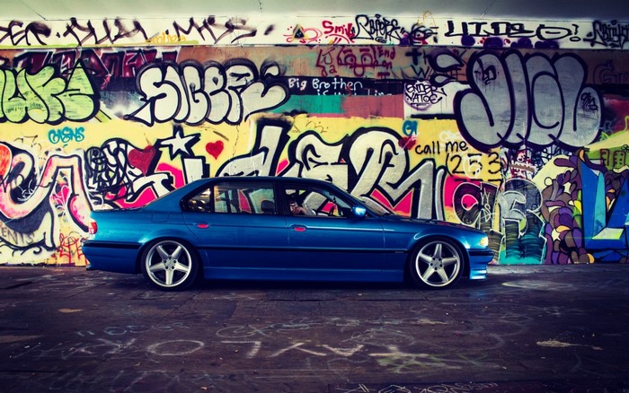Blue BMW car parked in front of graffiti wall