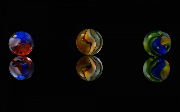 Three colorful glass marbles with reflections on black background